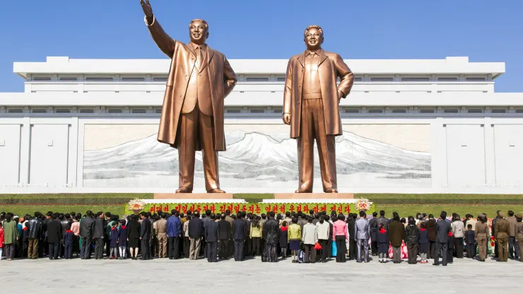 crowd standing next to statues in north korea